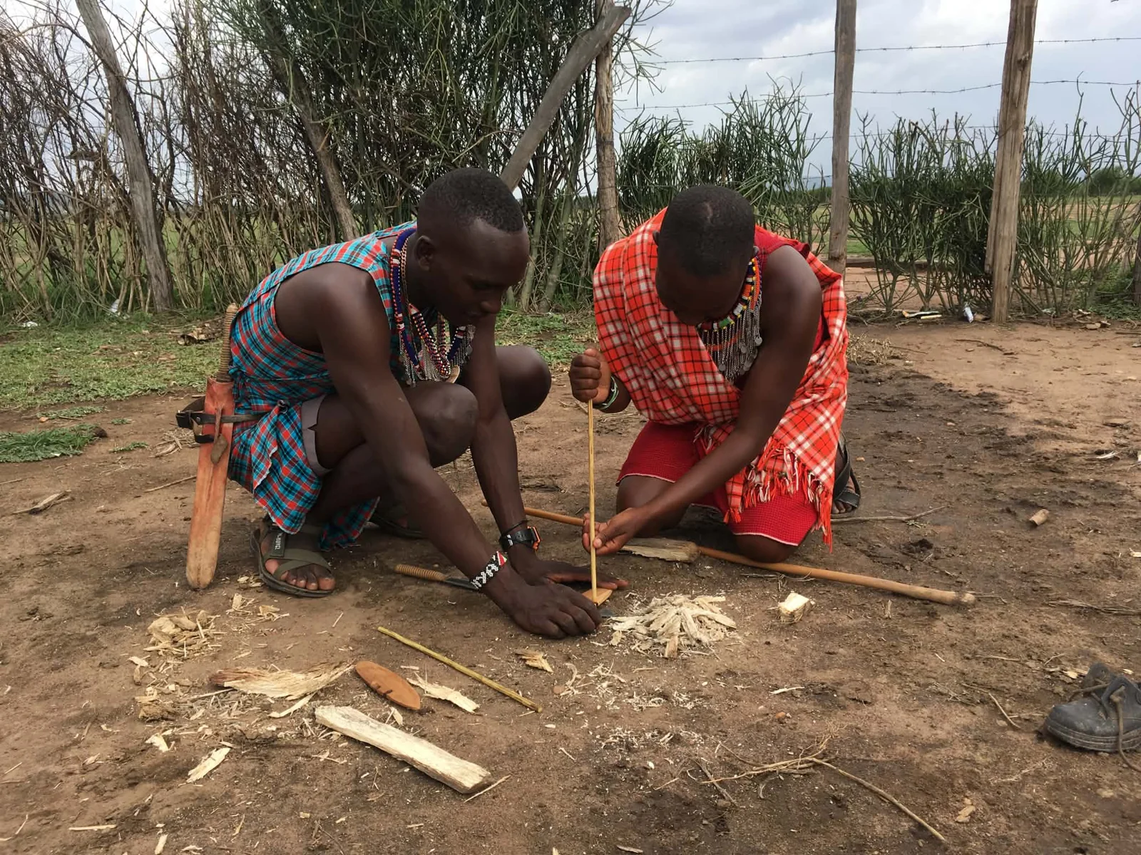 Two people handling wooden sticks on bare ground